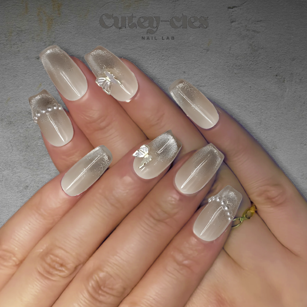 Elegant short square nude press-on nails with pearl accents and iridescent butterfly charm.