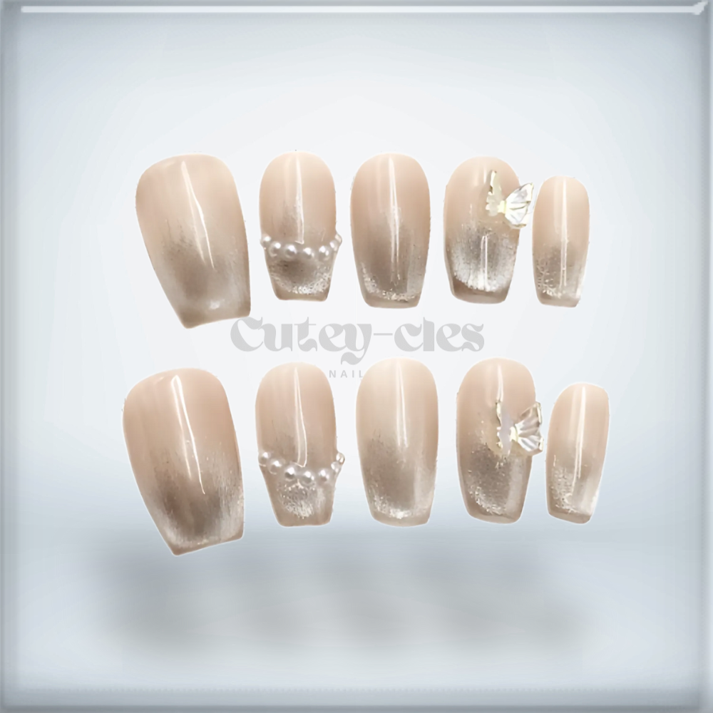 Elegant short square nude press-on nails with pearl accents and iridescent butterfly charm.