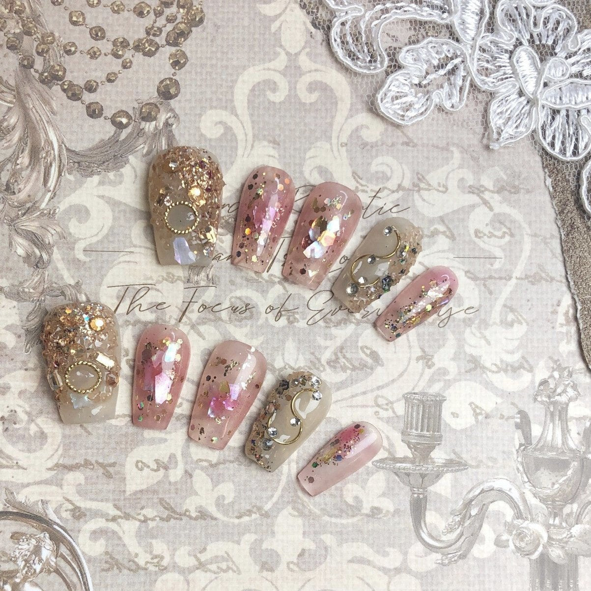 Luxurious medium coffin press-on nails with gold flakes, glitter, and metallic embellishments on a neutral base, featuring opulent, artistic designs for a glamorous look.