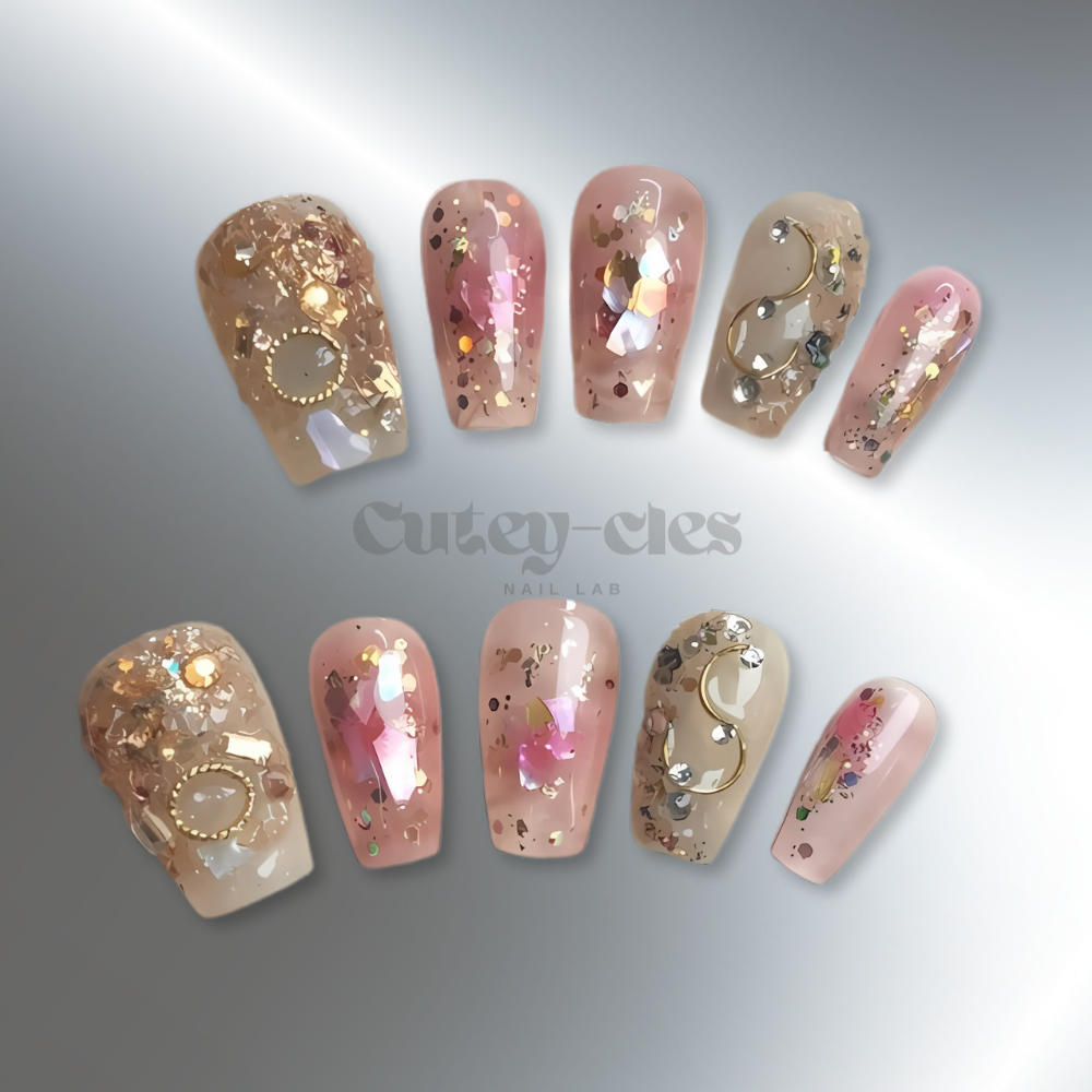 Luxurious high end press-on nails with gold flakes, glitter, and metallic embellishments on a neutral base, featuring opulent, artistic designs for a glamorous look.