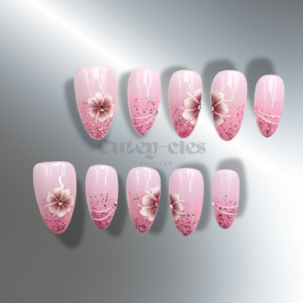 Pink almond press-on nails with glitter accents and 3D flower designs. Elegant, medium-length nails perfect for adding a touch of romance and sophistication to any look.