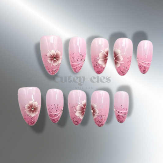 Pink almond press-on nails with glitter accents and 3D flower designs. Elegant, medium-length nails perfect for adding a touch of romance and sophistication to any look.