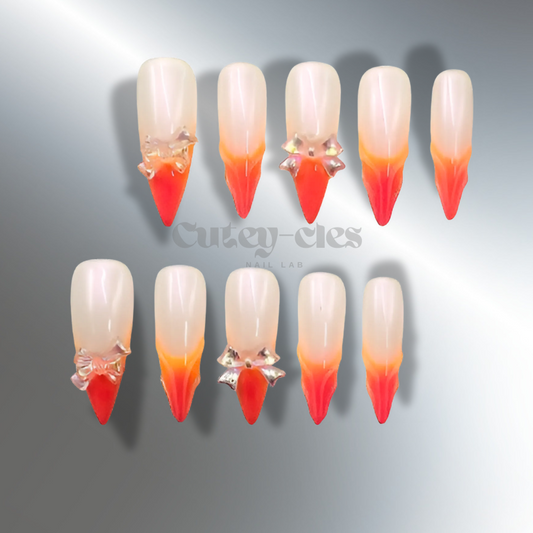 Fiery stiletto press-on nails with orange-to-red ombre gradient and 3D bow embellishments.