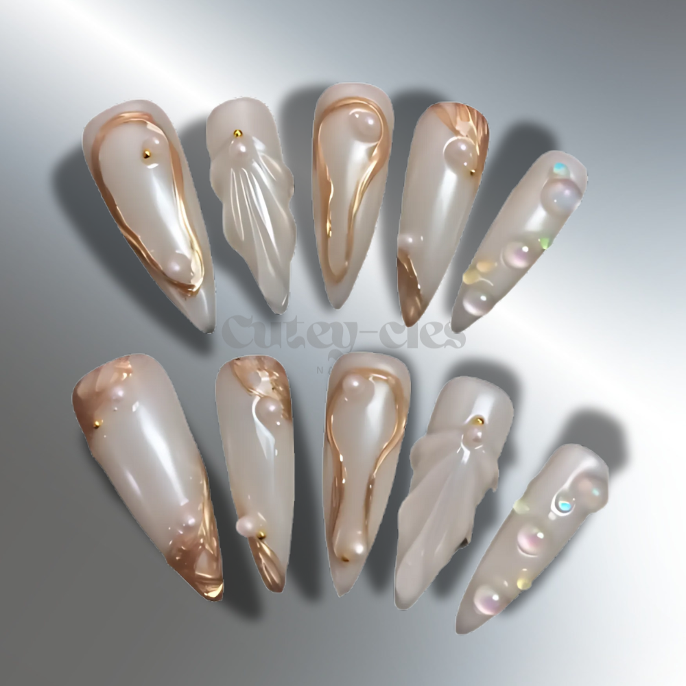 Long opalescent stiletto press-on nails with pearl-inspired finish, gold accents, and 3D embellishments. A luxurious nail design perfect for special events.