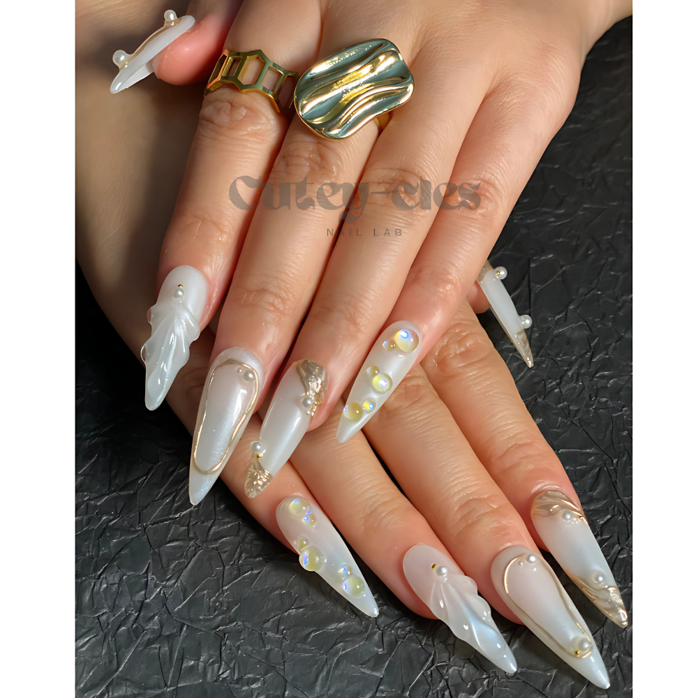 Long opalescent stiletto press-on nails for wedding, with pearl-inspired finish, gold accents, and 3D embellishments. A luxurious nail design perfect for special events.