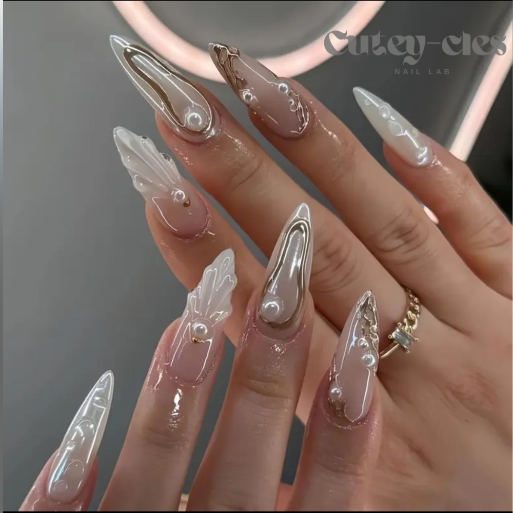 Long opalescent stiletto high end press-on nails with pearl-inspired finish, gold accents, and 3D embellishments. A luxurious nail design perfect for special events.