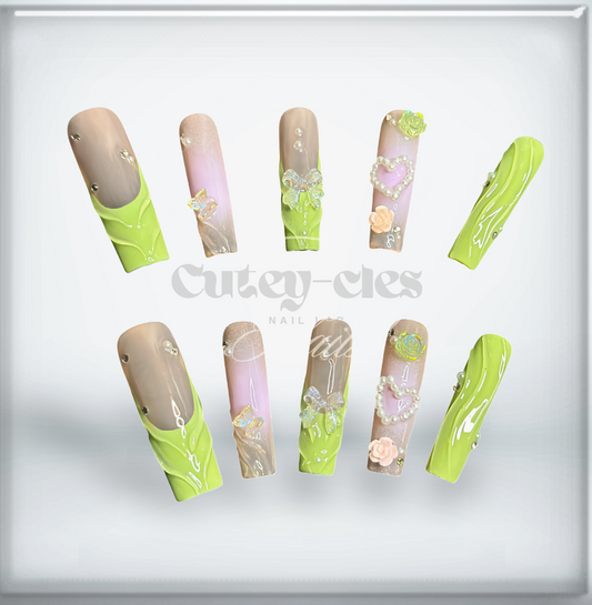 Long pastel green and nude press-on nails with 3D pearls, bows, hearts, and floral designs in a coffin shape.