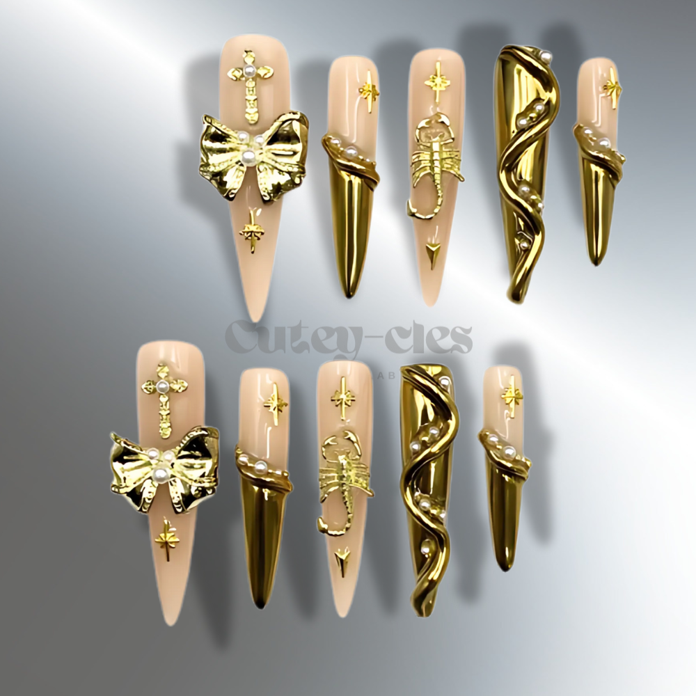 Long stiletto press-on nails with gold metallic sculpted designs, gothic star motifs, pearl accents, and a translucent base for an elegant and bold look.