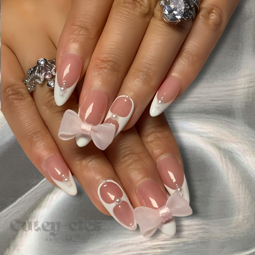 White French tip almond press-on nails with pink bows and pearl accents, ideal for a feminine and elegant look.