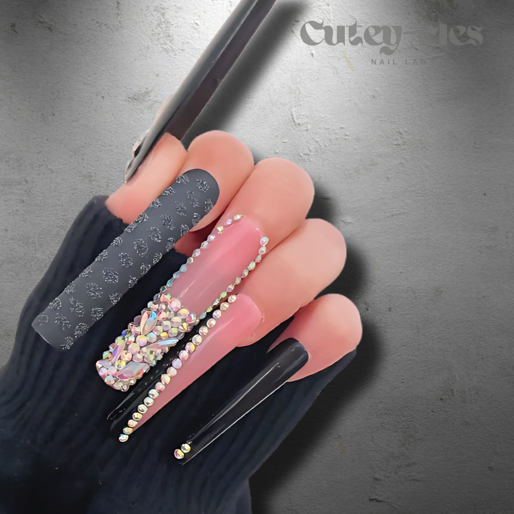 Close-up of 3XL black and pink rhinestone press-on nails worn on a hand with jewelry.