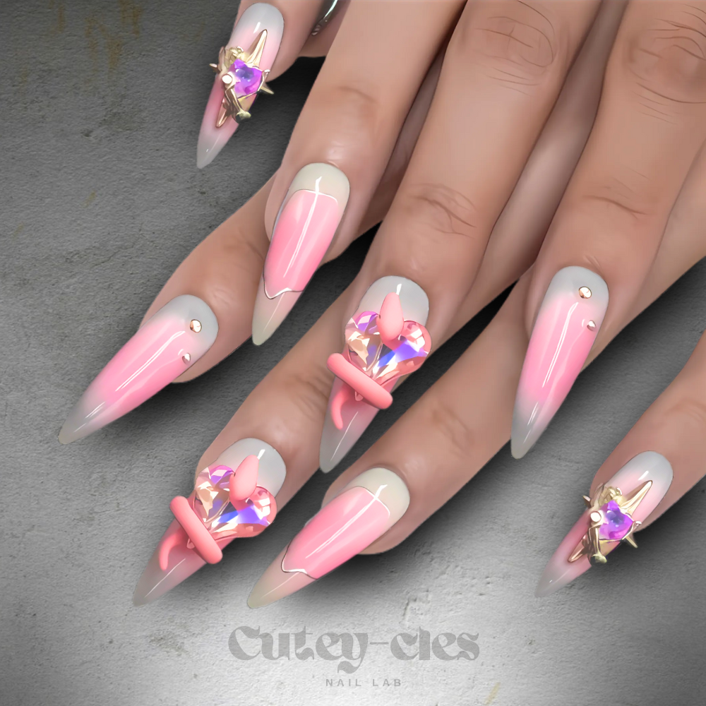 Pink gradient press-on nails with crystal heart embellishments and metallic star accents.