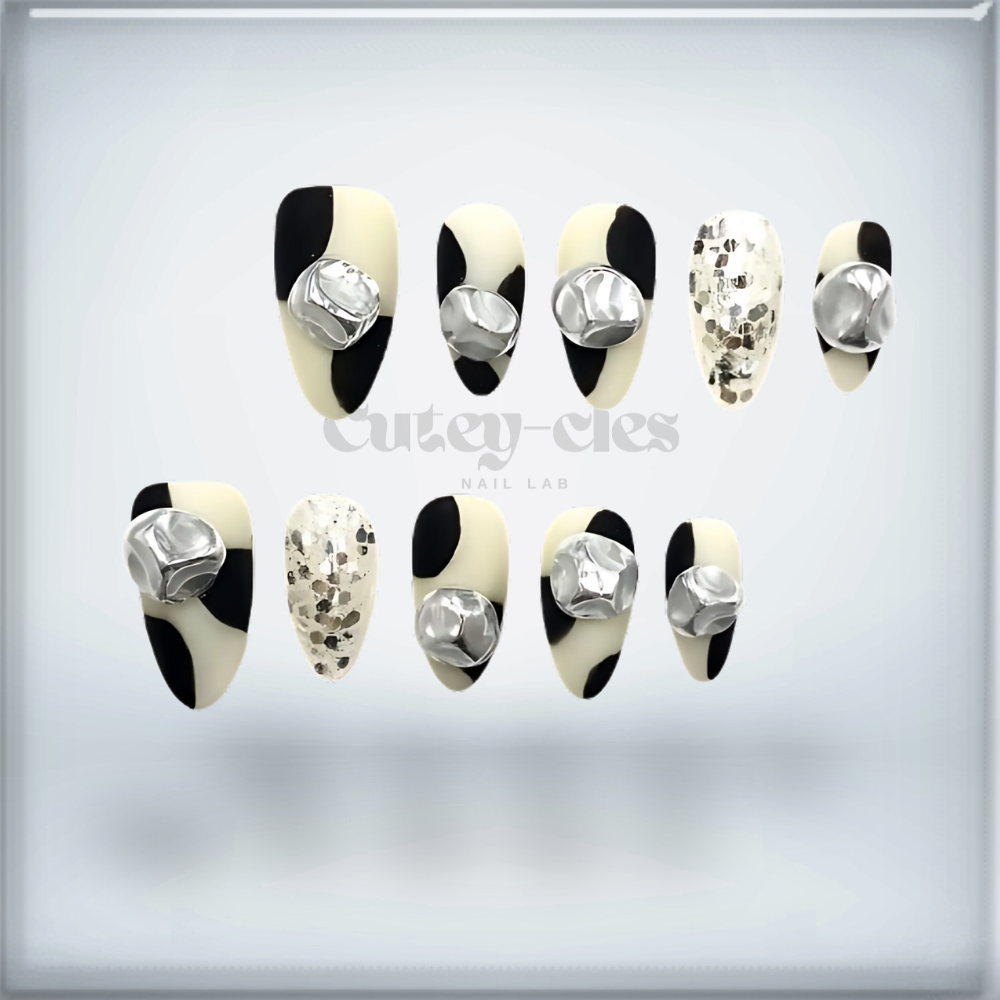 Short almond press-on nail set featuring a black-and-white monochrome design with 3D metallic embellishments.