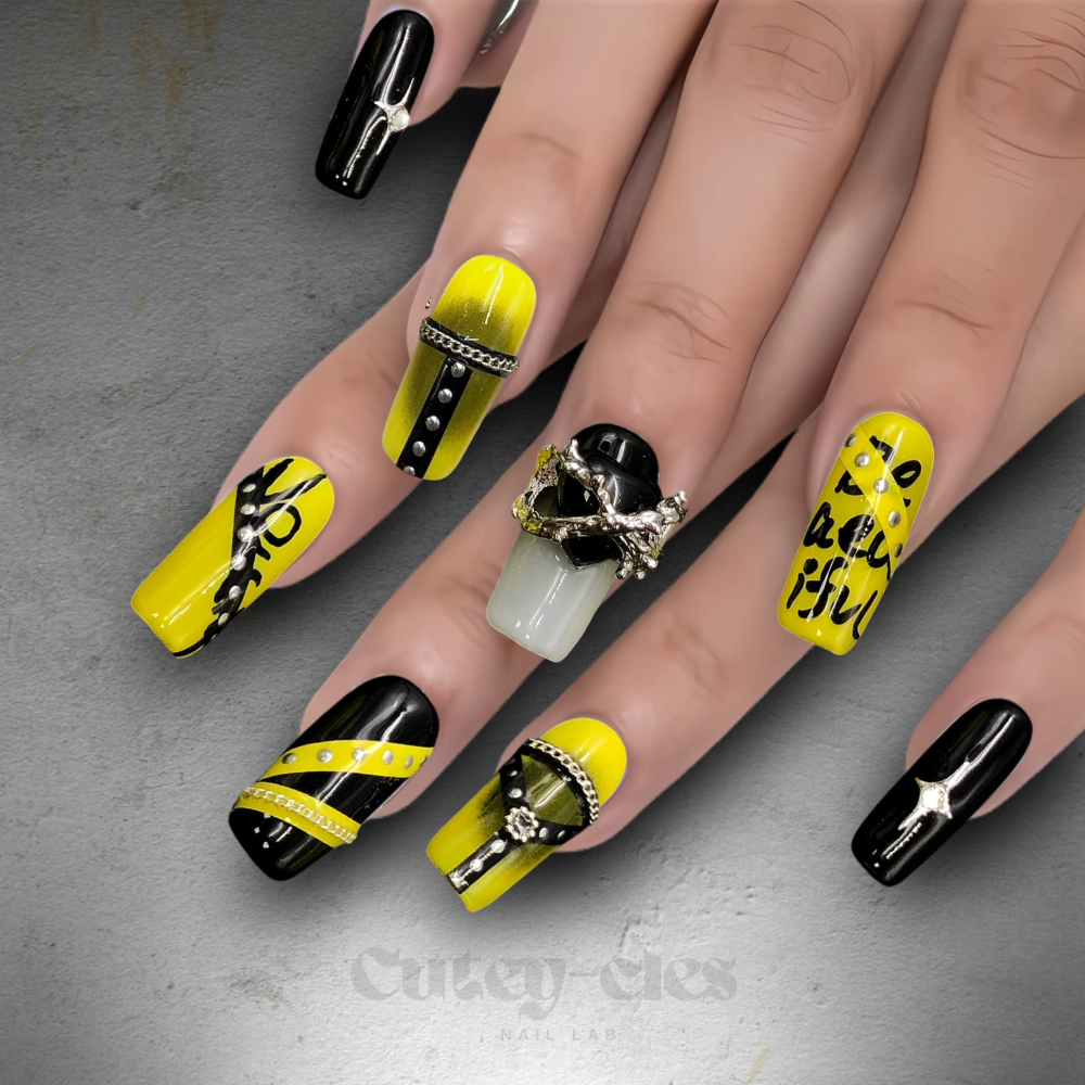 Long square press-on nail set showcasing bold black and yellow designs with metallic chains and statement charms.