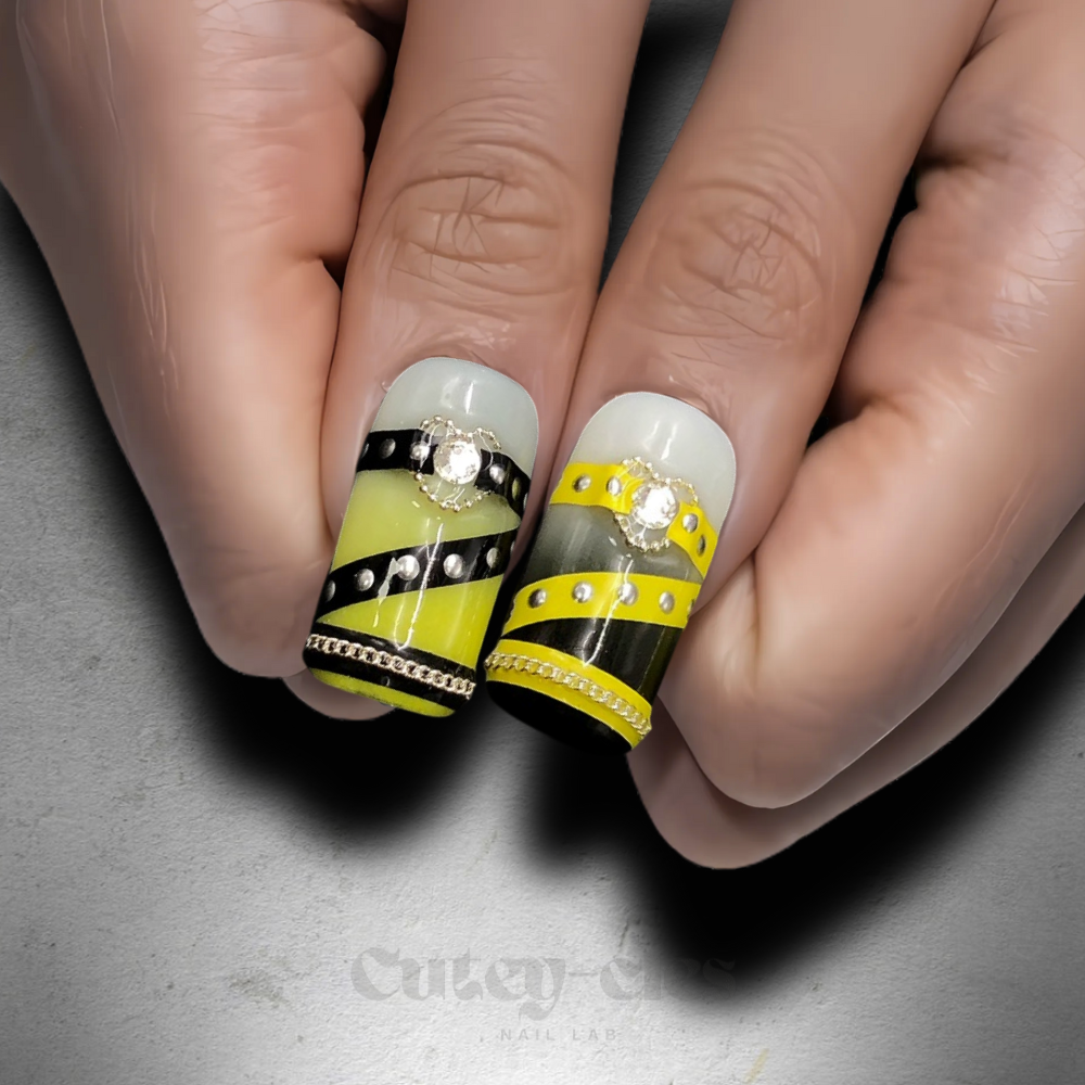 Long square press-on nail set showcasing bold black and yellow designs with metallic chains and statement charms.