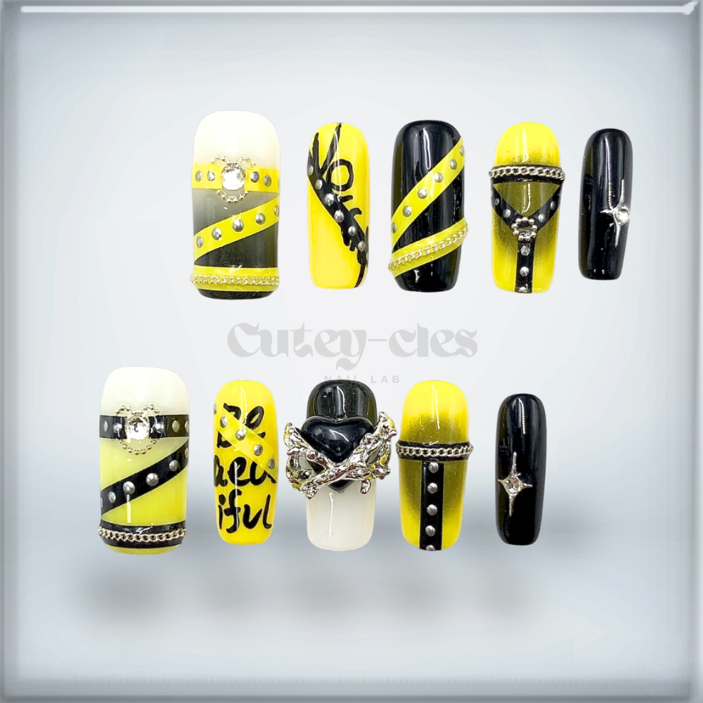 BDSM inspired press-on nail set showcasing bold black and yellow designs with metallic chains and statement charms.