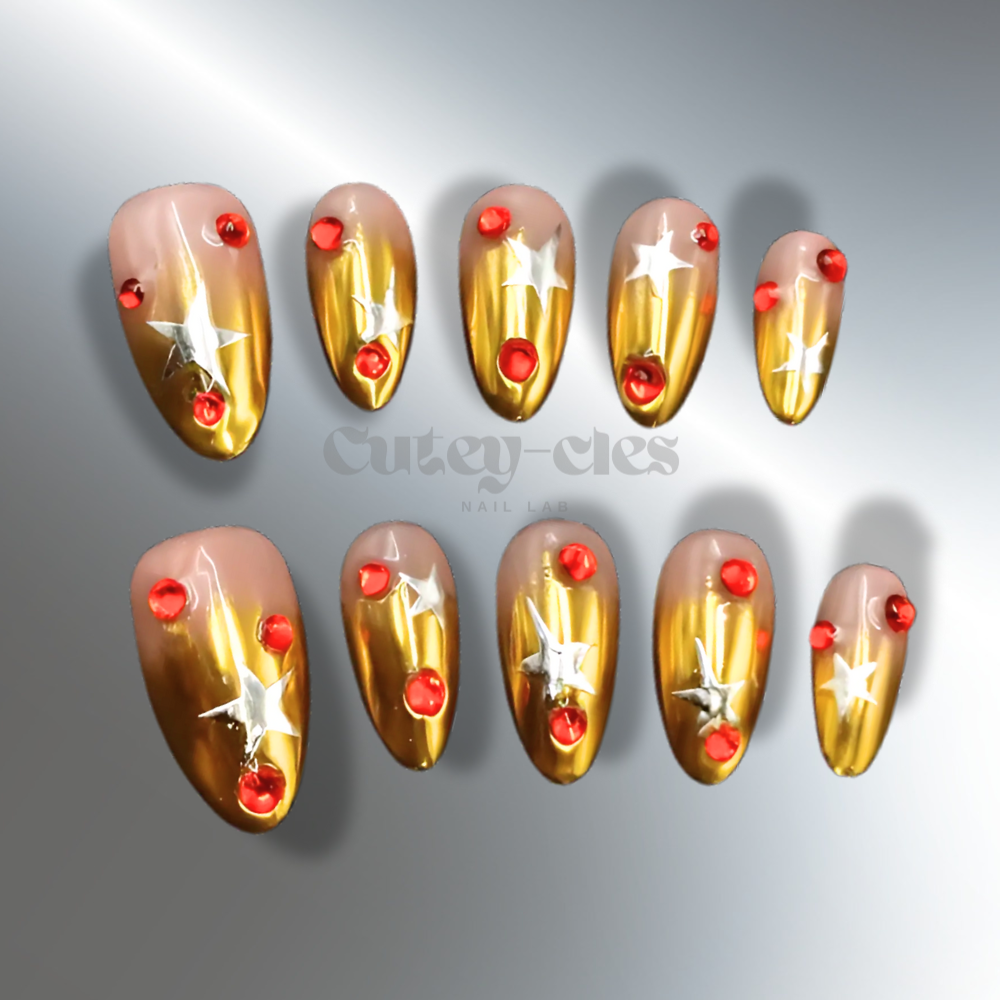 Gold chrome press-on nails in almond shape, decorated with silver stars and red gemstones, designed for a festive holiday look.