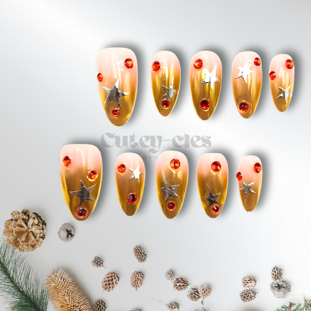 Gold chrome press-on nails in almond shape, decorated with silver stars and red gemstones, designed for a festive holiday look.