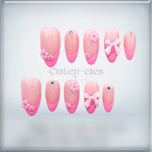 Press-on nails with pink French tips, floral decorations, bows, and gems for a cute and feminine look.