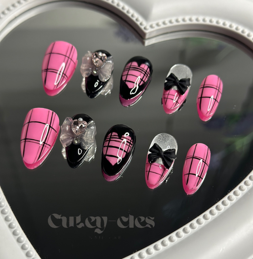 almond press-on nails featuring a pink and black plaid pattern with glossy finishes, bow embellishments, and heart details.