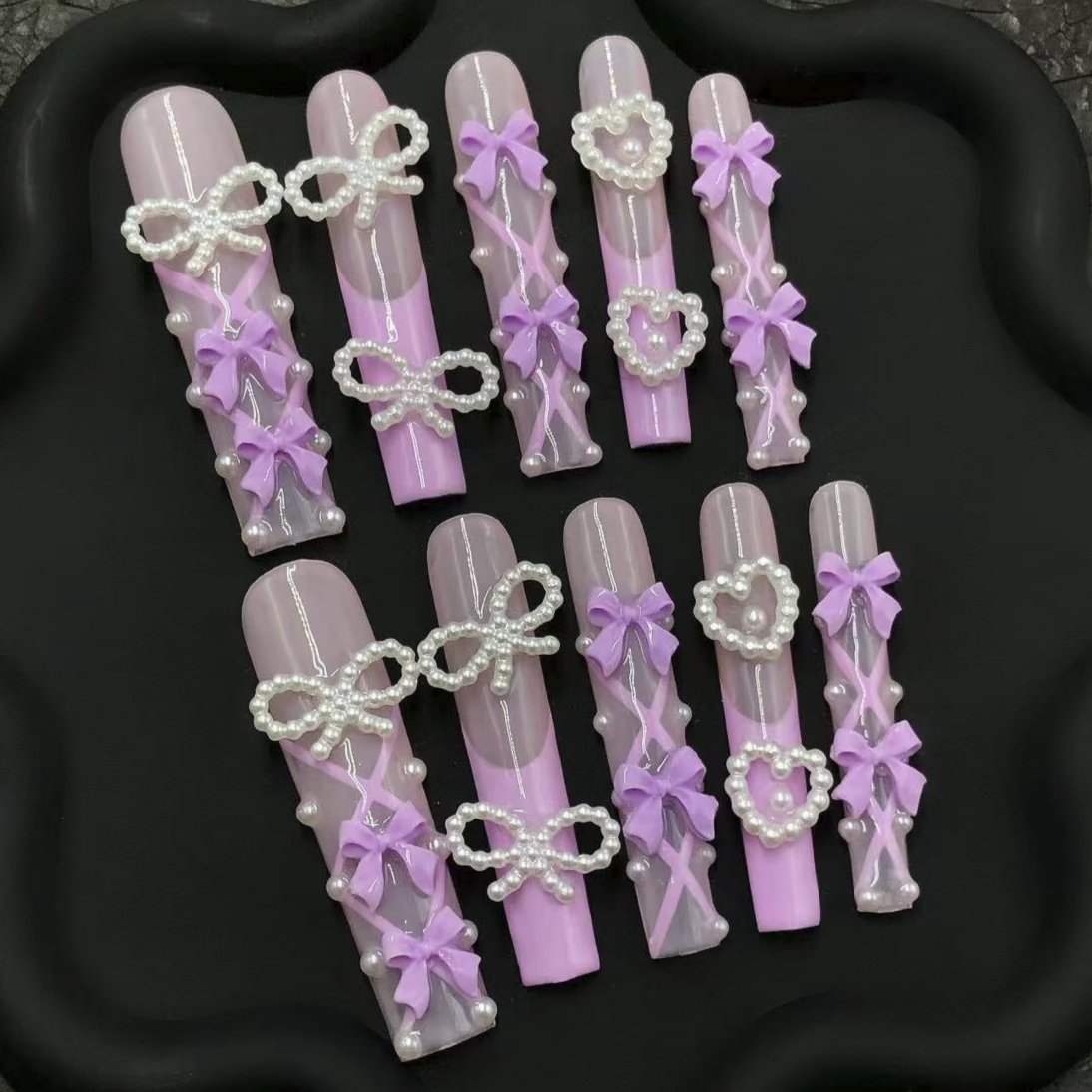 Pastel pink and lavender press-on nails with 3D bow and pearl accents for a cute, feminine look.