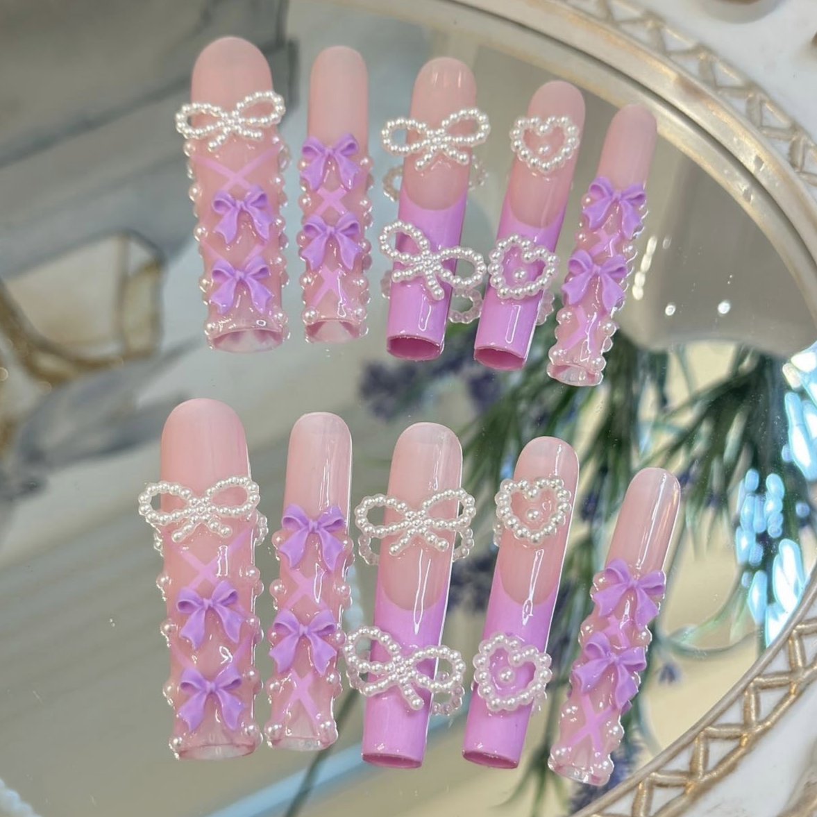 Pastel pink and lavender press-on nails with 3D bow and pearl accents for a cute, feminine look.