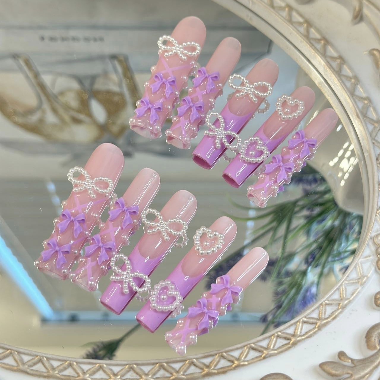 Pastel pink and lavender press-on nails with 3D bow and pearl accents for a cute, feminine look.