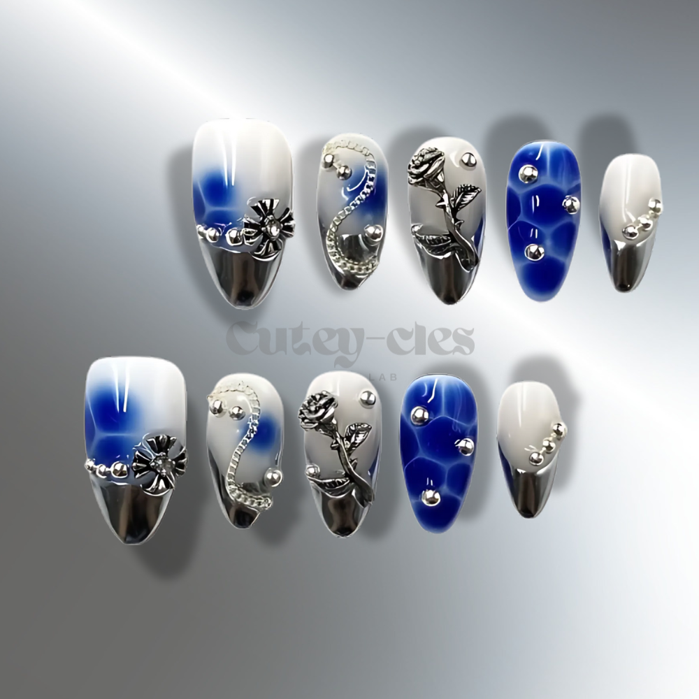 Blue and silver almond press on nails with 3D floral accents, metallic silver details, and a blue gradient. Elegant medium-length nails featuring intricate rose and flower designs for a sophisticated look.