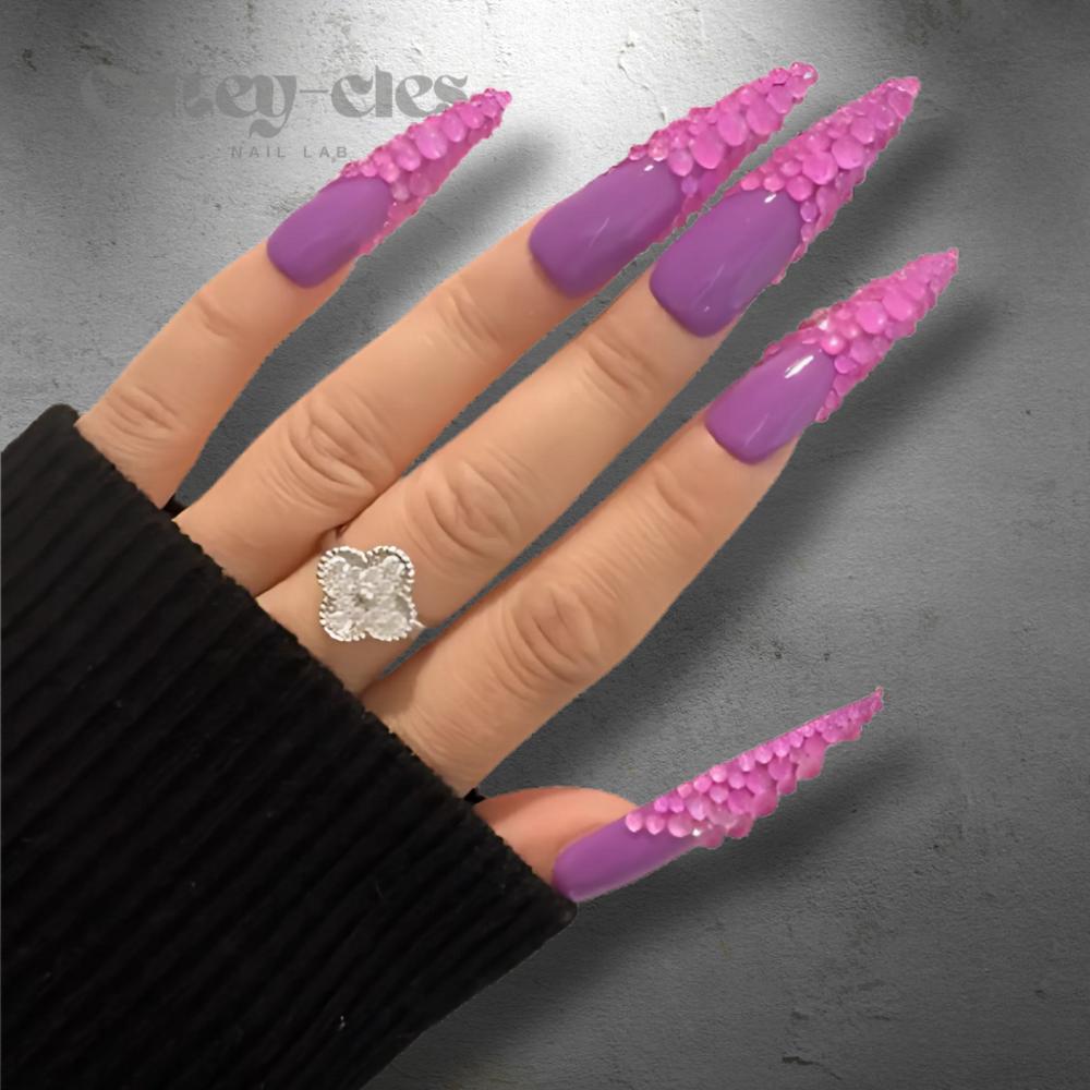 Vibrant 3D purple rhinestone stiletto nails, showcasing luxurious design with high-gloss polish and bold crystal embellishments