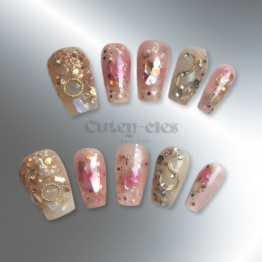 Luxurious high end press-on nails with gold flakes, glitter, and metallic embellishments on a neutral base, featuring opulent, artistic designs for a glamorous look.